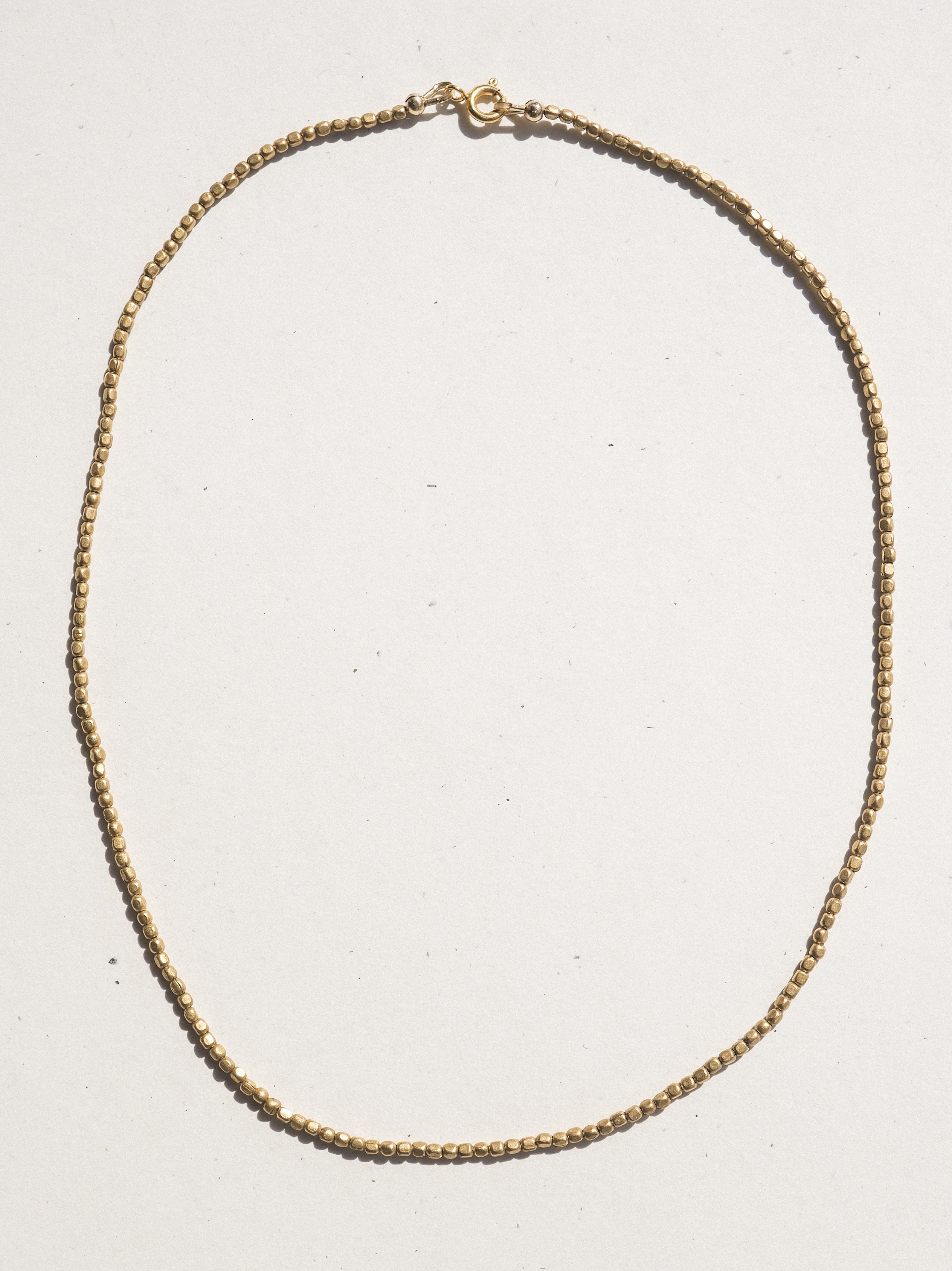 A delicate bronzechain necklace with a small lobster clasp, laid flat on a light off-white background.