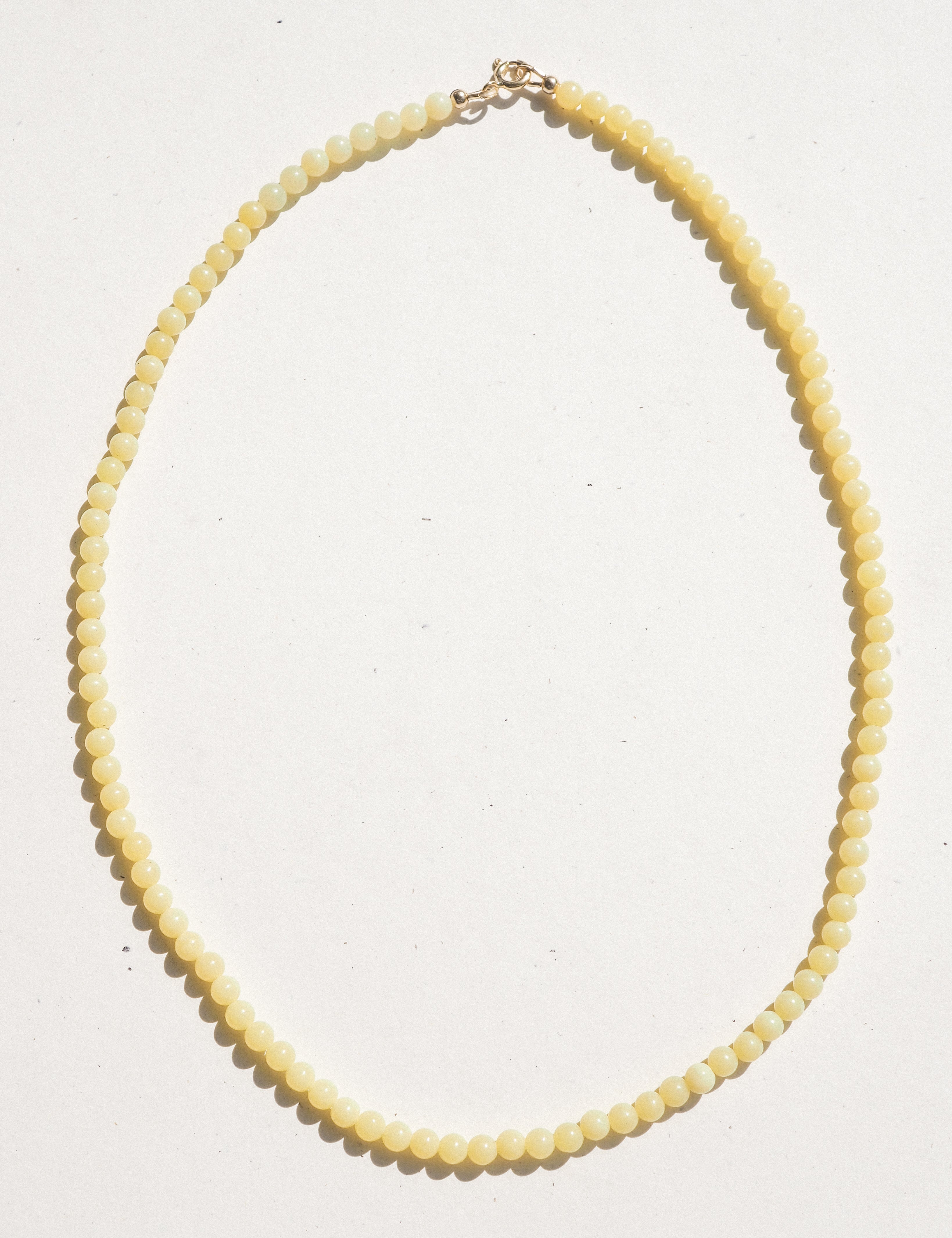 A pale yellow beaded necklace with a small gold clasp, laid flat on a white background.