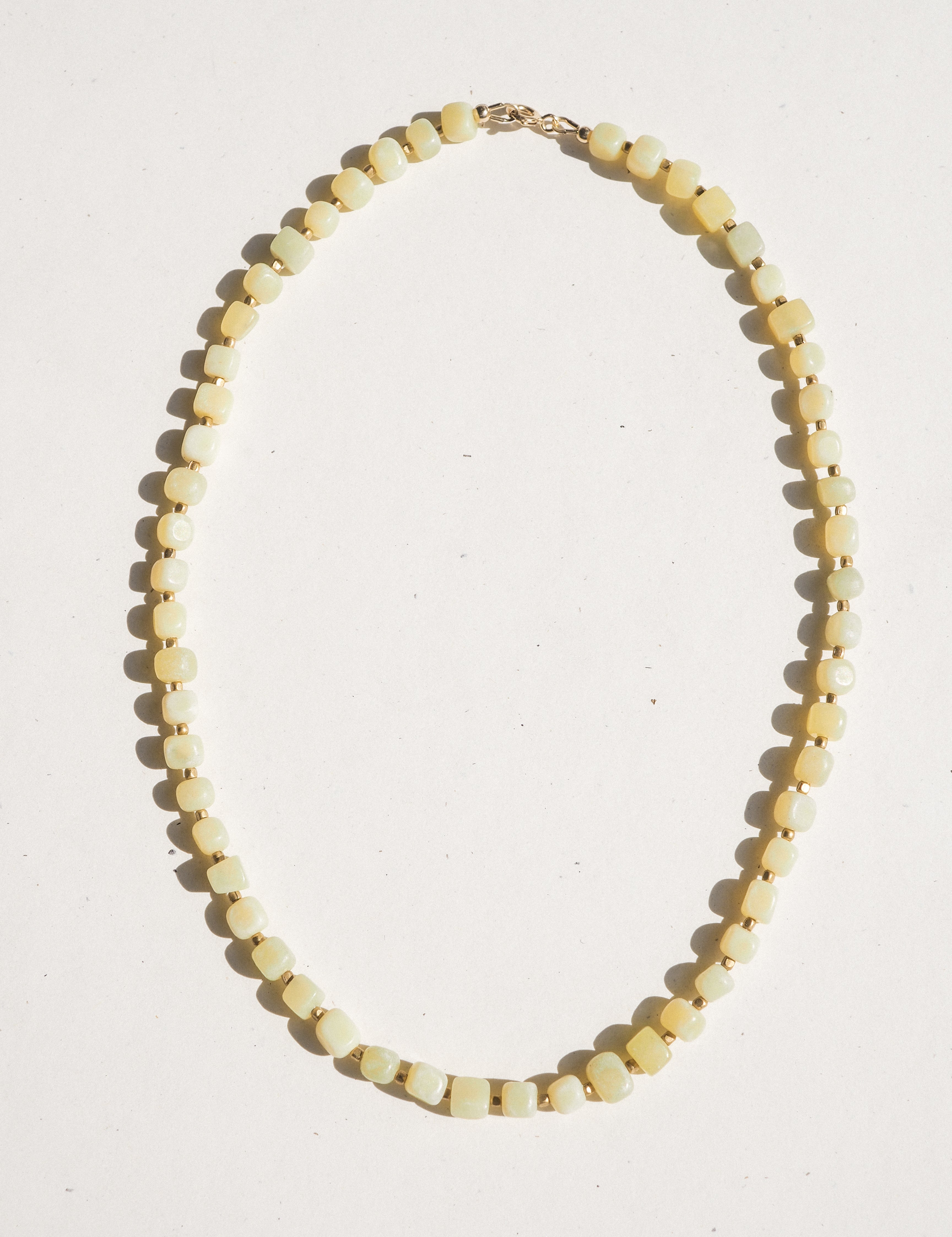 A beaded necklace made of small, faceted pale yellow beads separated by tiny gold spacer beads, with a gold clasp, laid out on a plain white background.