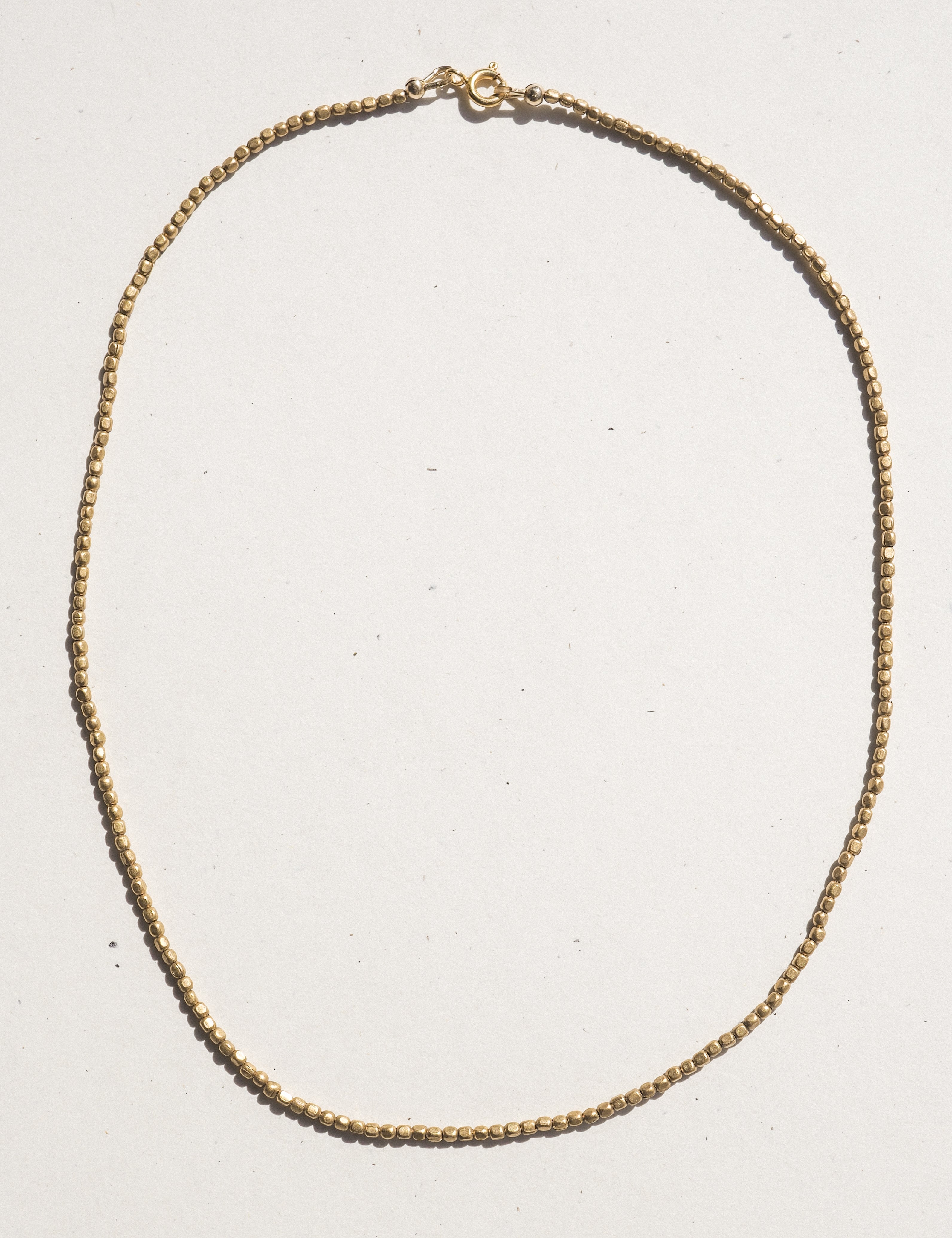A delicate bronzechain necklace with a small lobster clasp, laid flat on a light off-white background.