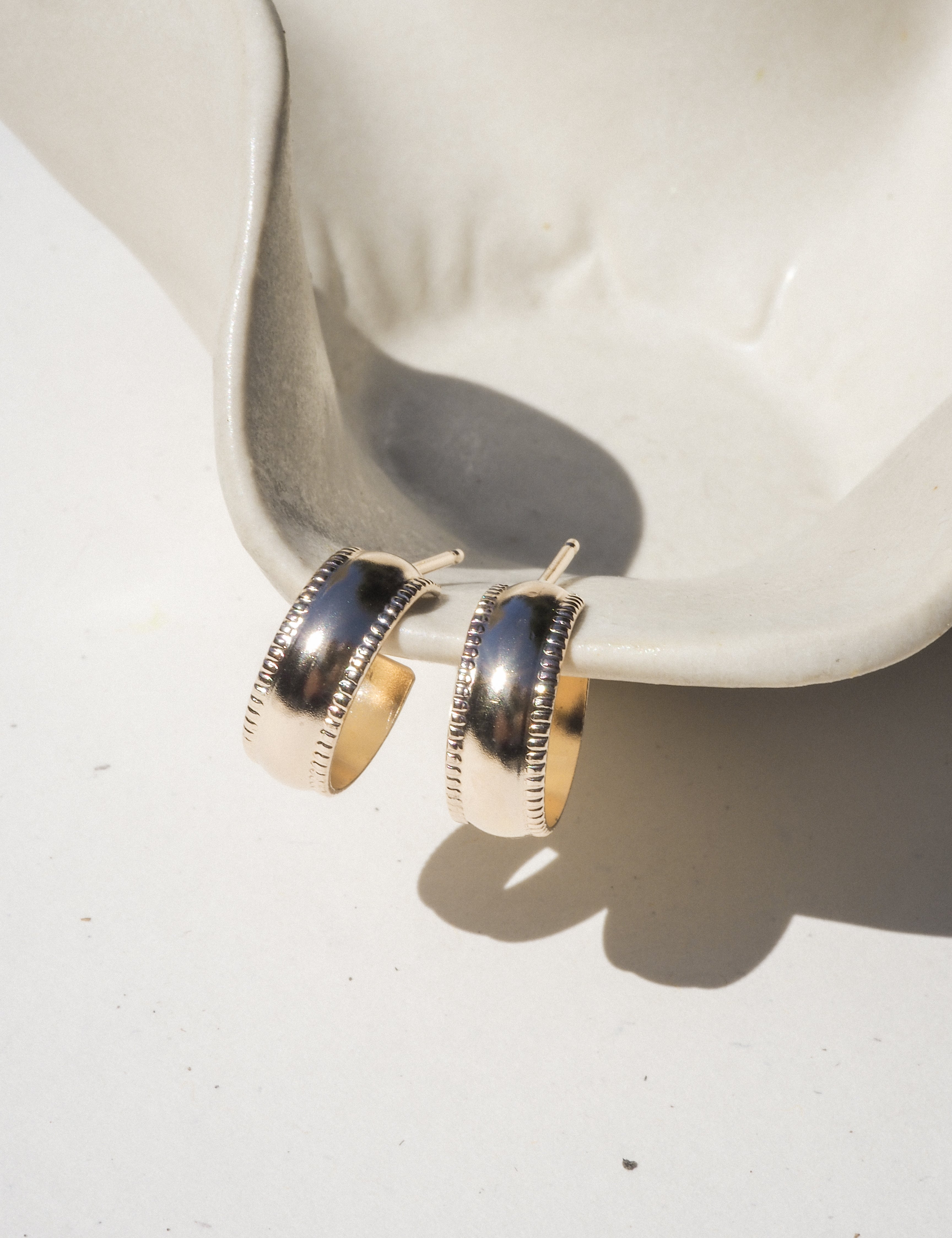 Gold hoop earrings with a pattern on a white dish