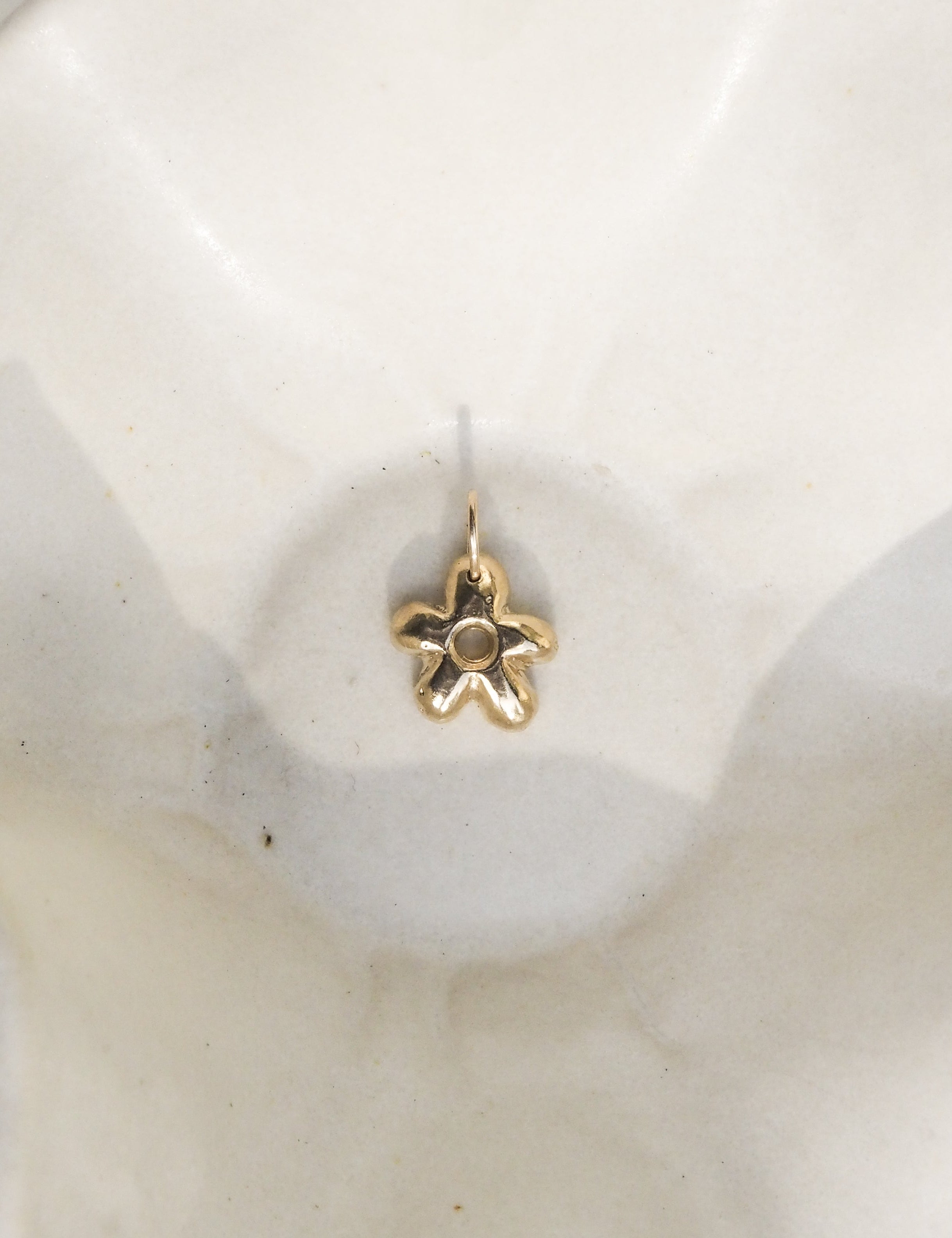 A small gold flower-shaped earring with a central round stone, displayed on a white ceramic dish.