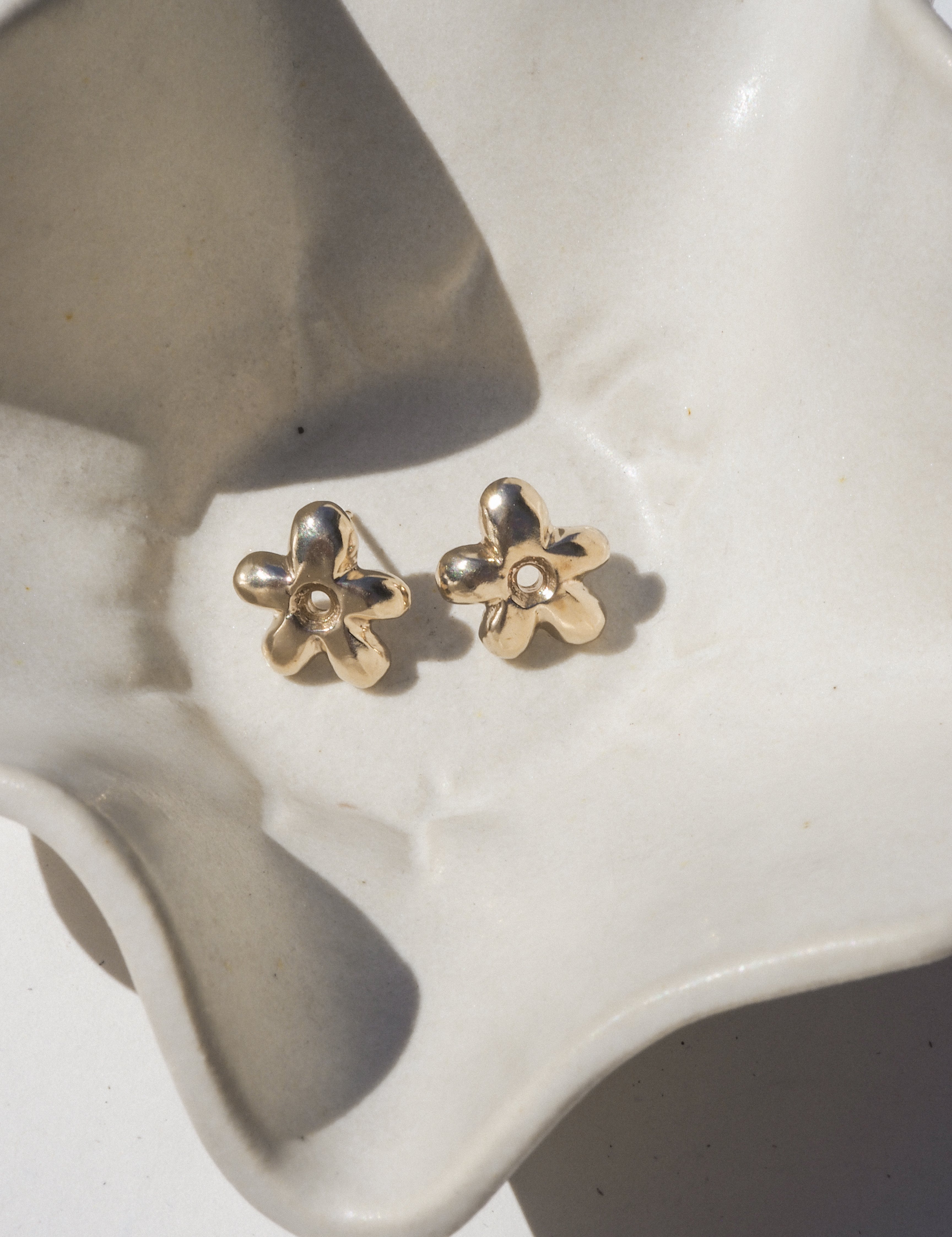 Gold flower-shaped earrings on a white ceramic dish