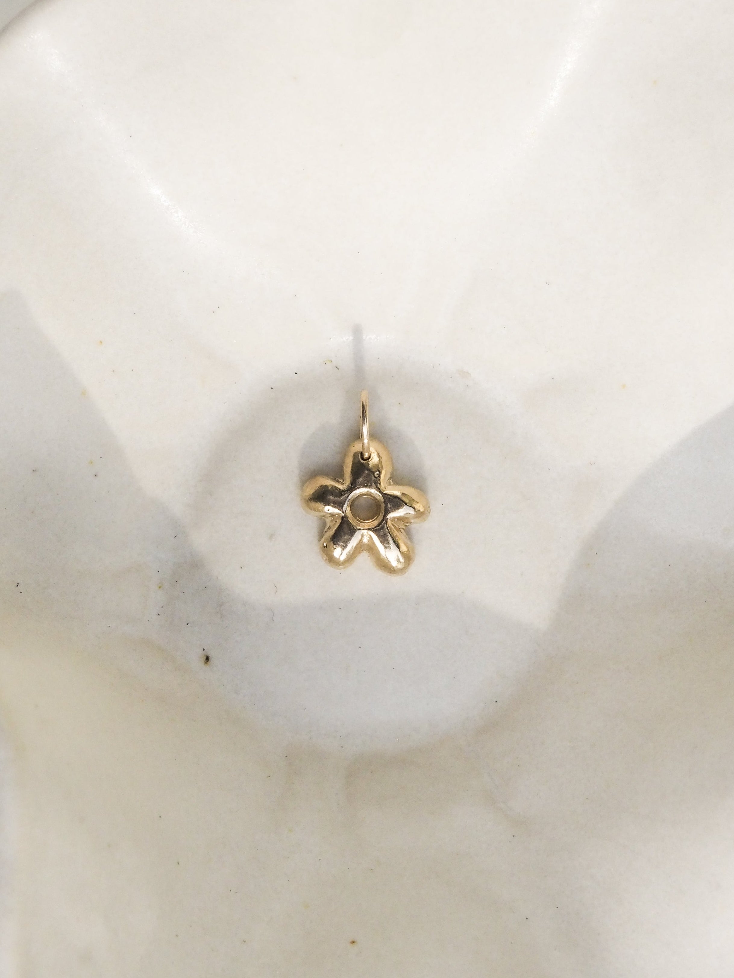 A small gold flower-shaped earring with a central round stone, displayed on a white ceramic dish.