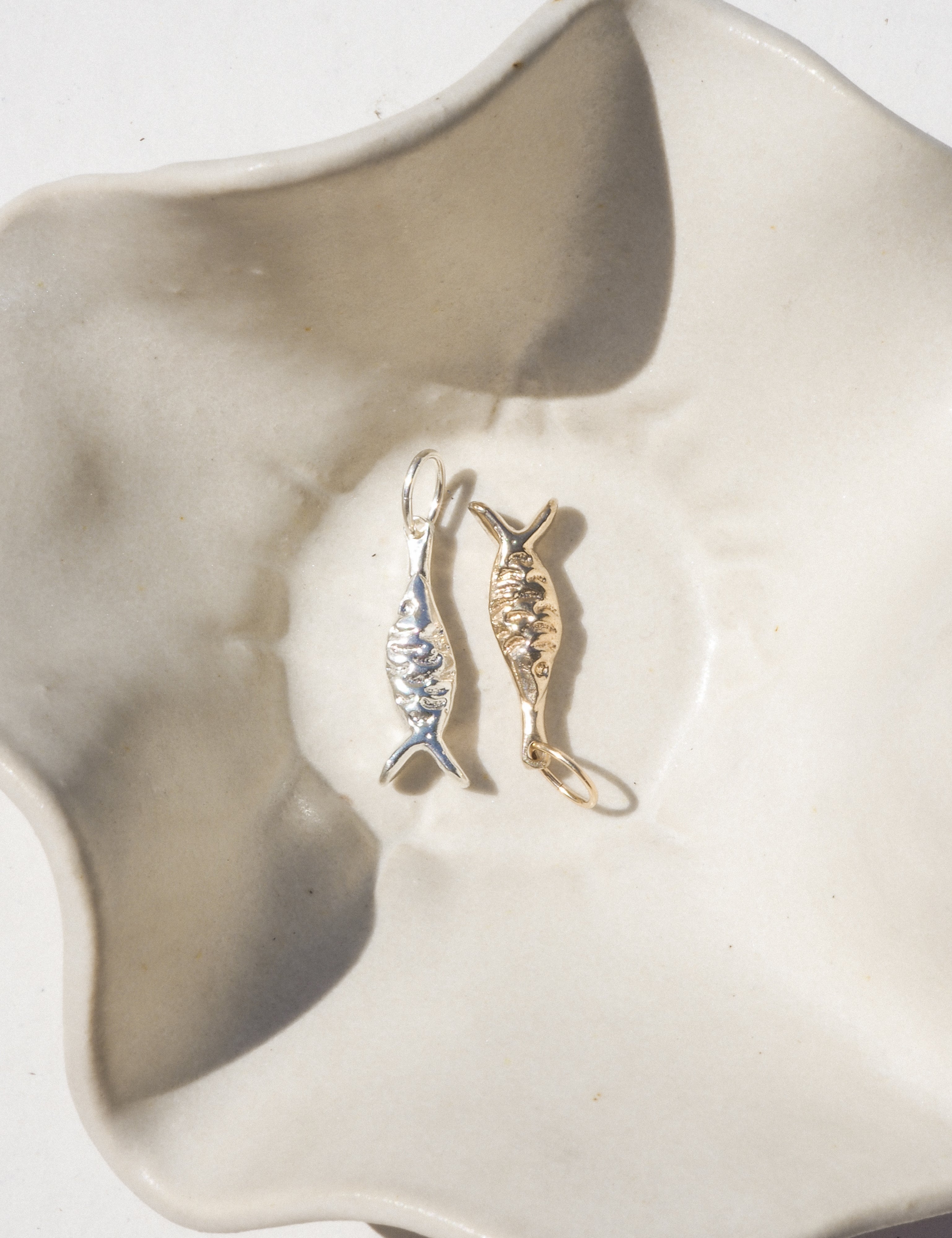 Gold and silver fish-shaped earrings on a white shell.